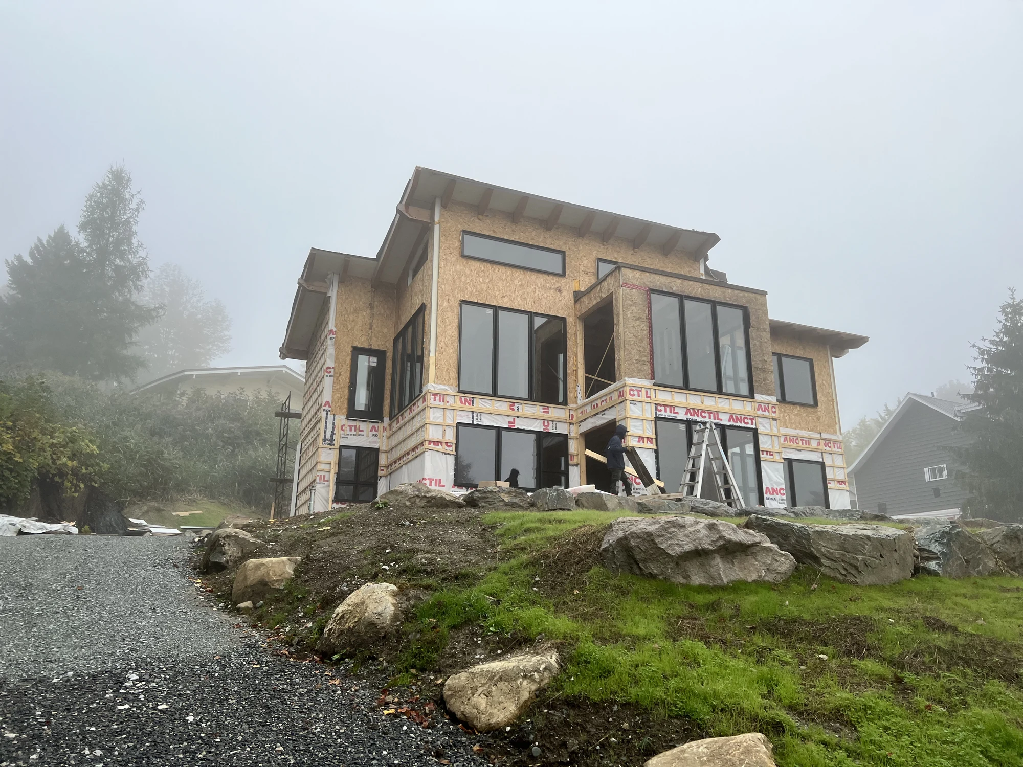 Résidence en construction dans la brume avec grandes fenêtres et parement de bois