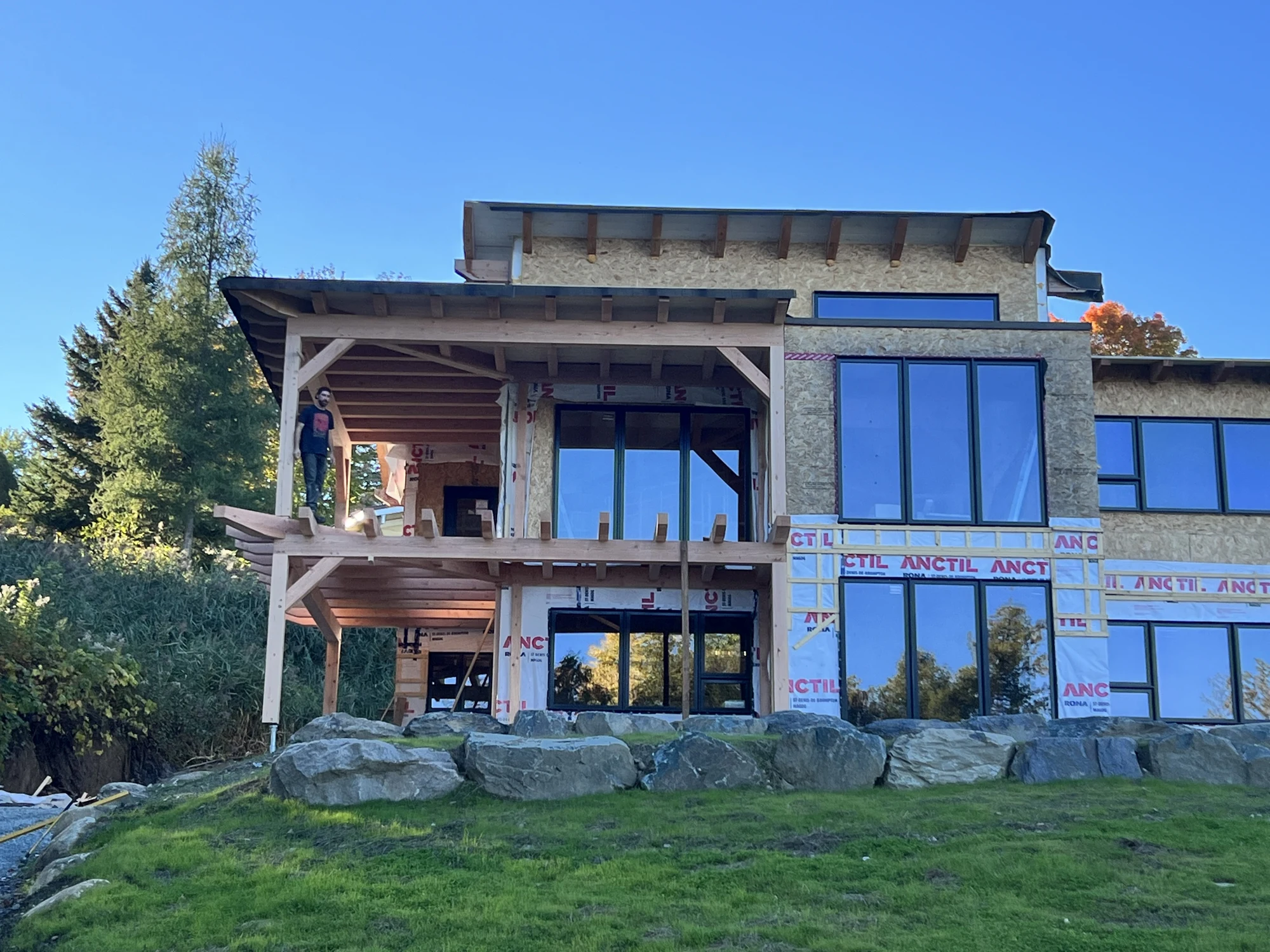 Façade de la résidence en chantier avec grandes fenêtres et structure de terrasse en bois