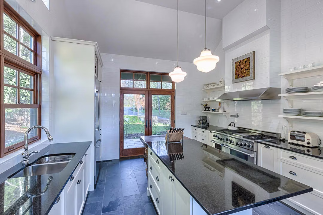 Vue de la cuisine avec évier sous la fenêtre, îlot central et cuisinière